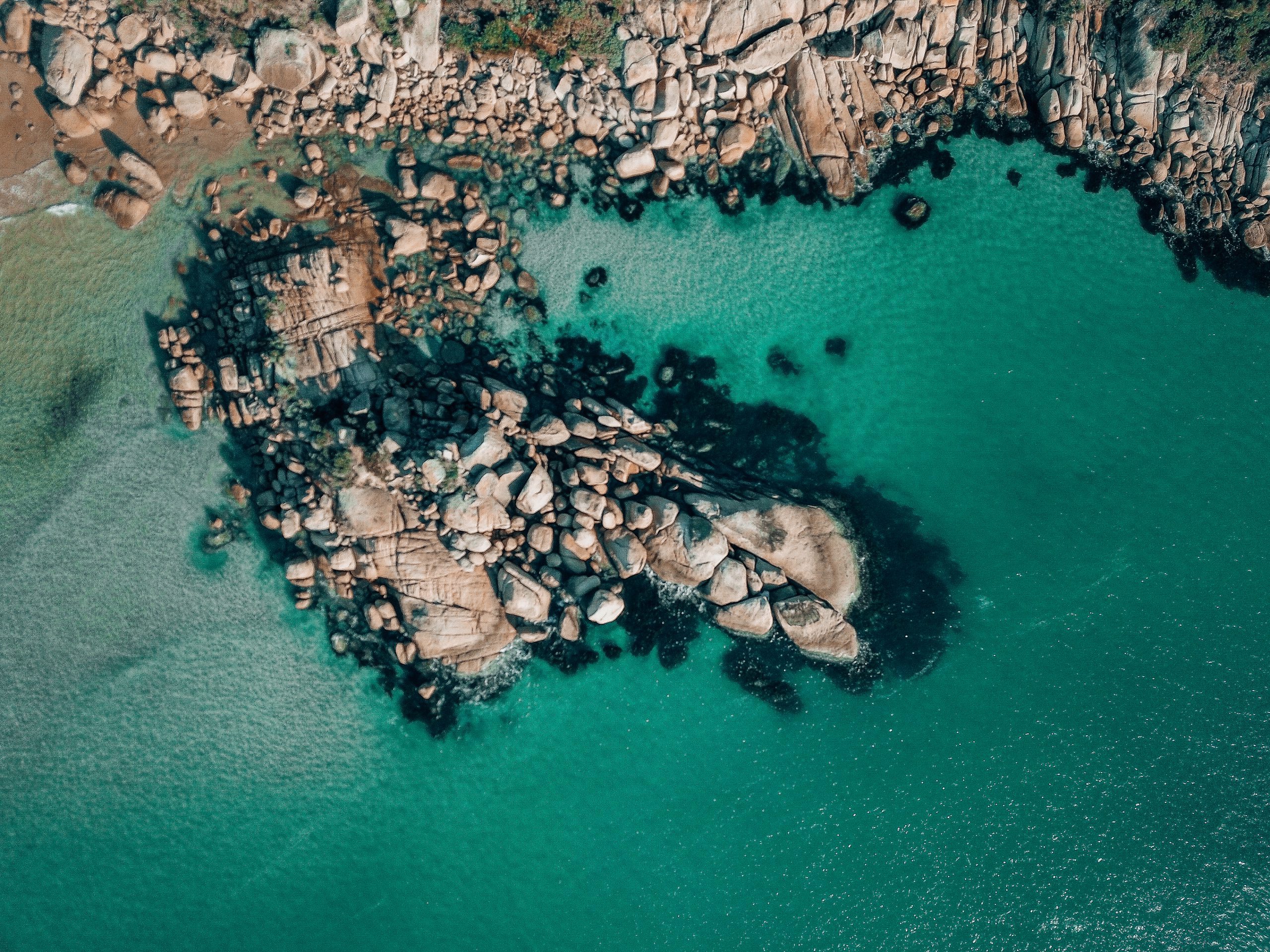 An aerial view of a rocky cove with grey rocks dotted in the clear blue turquoise ocean.