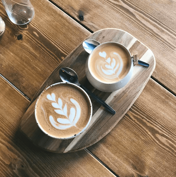two coffees with latte art in mugs on a wooden tray