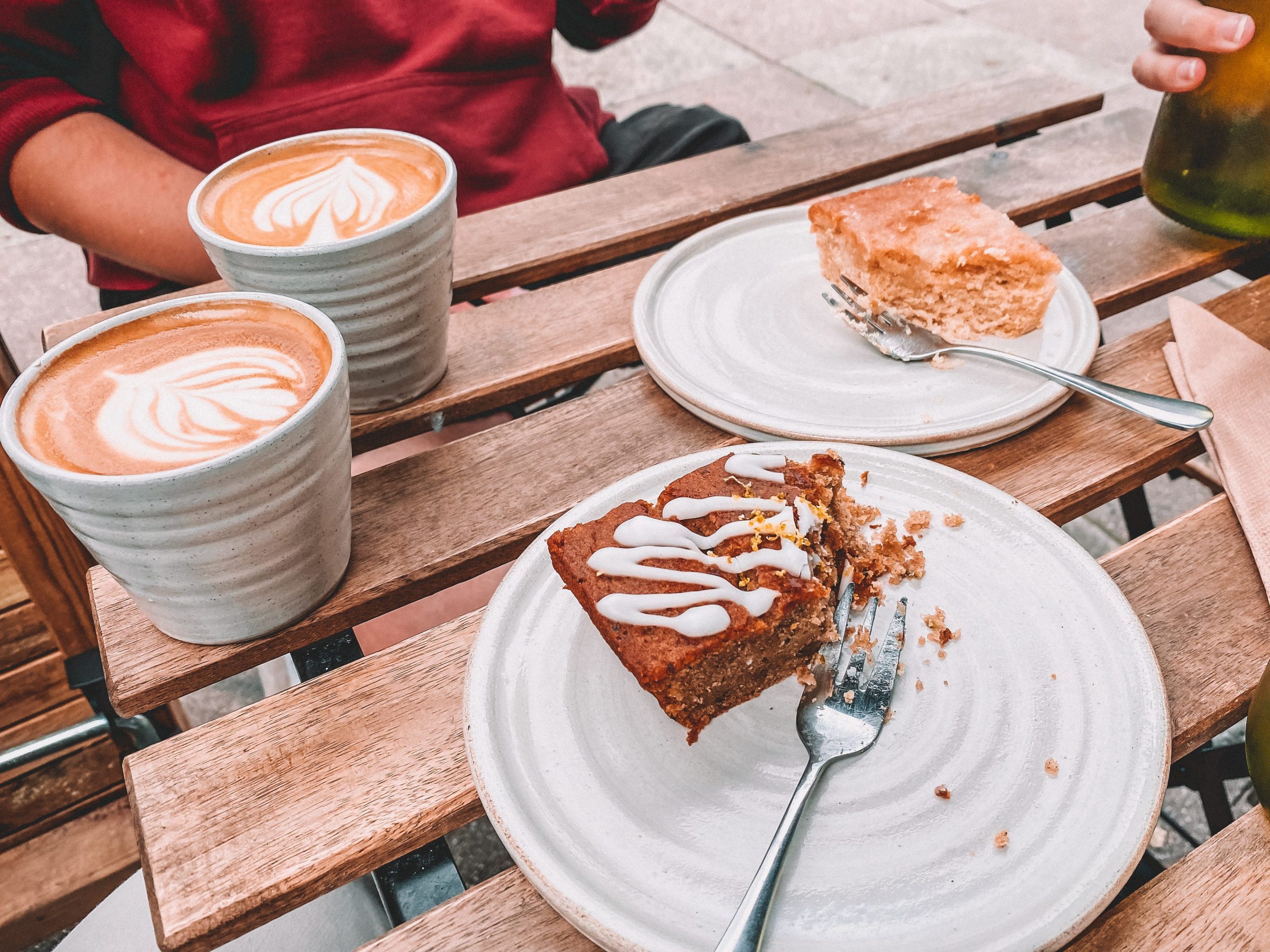 cakes on ceramic plates and flat whites in mugs on an outdoor wooden table