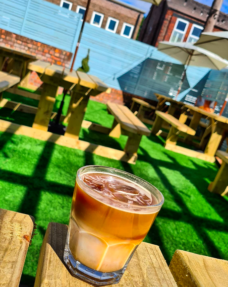an iced coffee in a glass on a wooden bench in an outdoor seating area