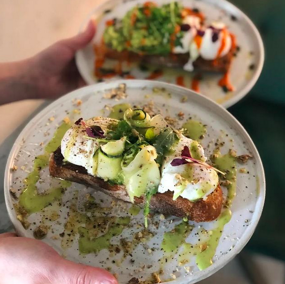 a person holding two breakfast dishes containing sourdough toast, poached eggs and vegetables