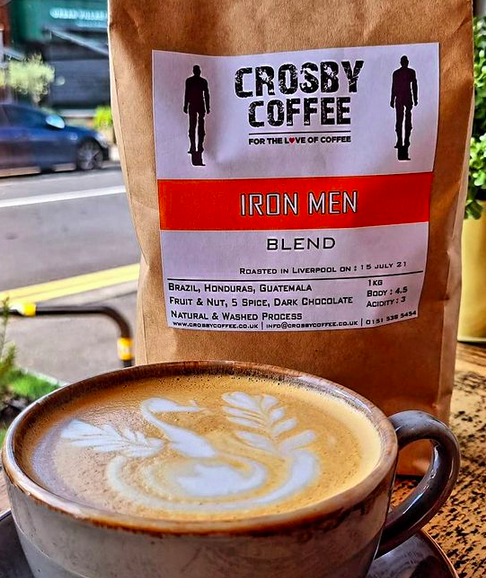 a coffee in a mug with latte art in front of a bag of crosby coffee beans