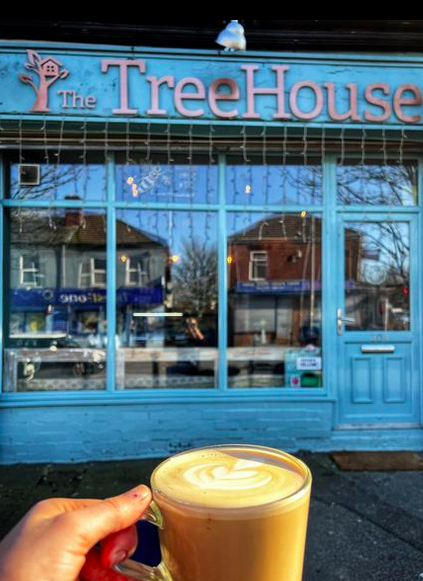 person holding latte outside treehouse cafe in broughton