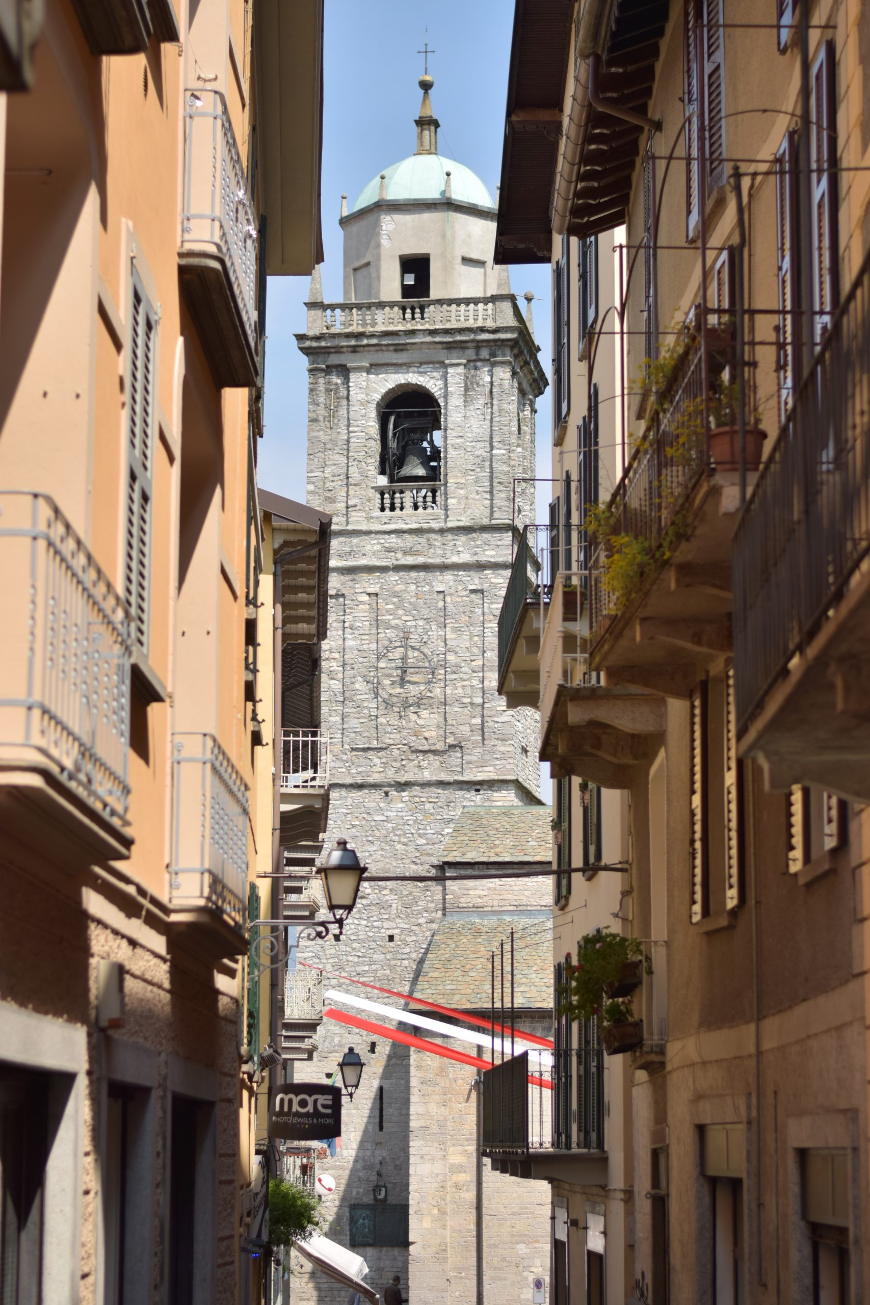 A narrow street of terracotta buildings with balconies and french shutters with a tall bell tower at the end