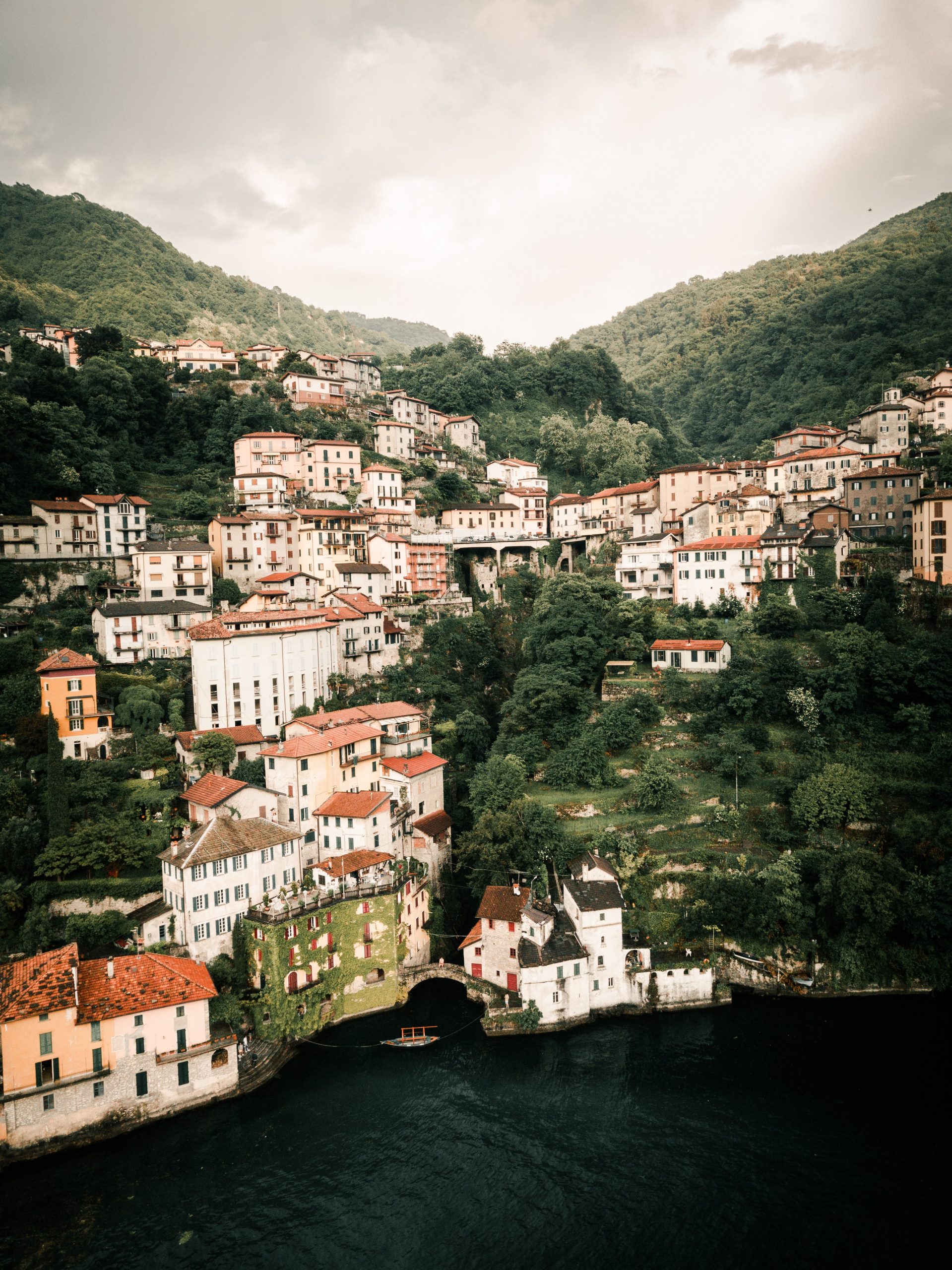 A hillside town with terracotta roofed buildings and a lush gorge in the middle running down to a lake.