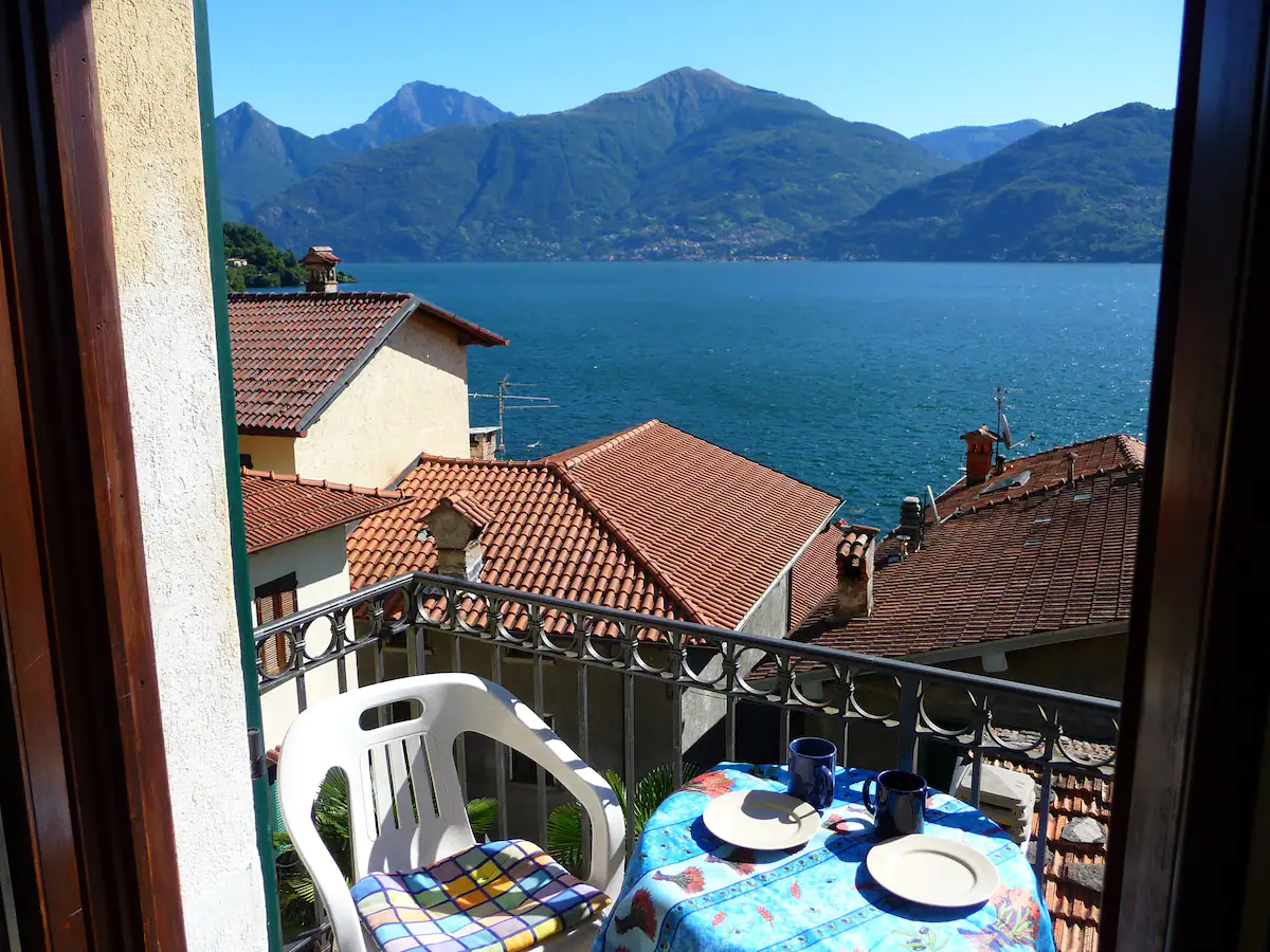 a table set with crockery and a plastic chair on a balcony overlooking a lake and mountains