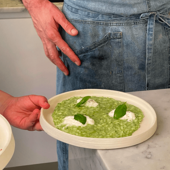 a dish of green risotto on a marble surface with a person in a blue apron behind it