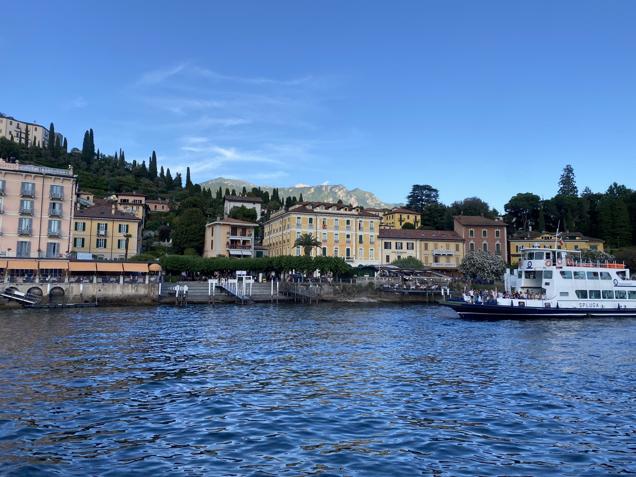 An italian town with a lake in the foreground and a ferry departing.