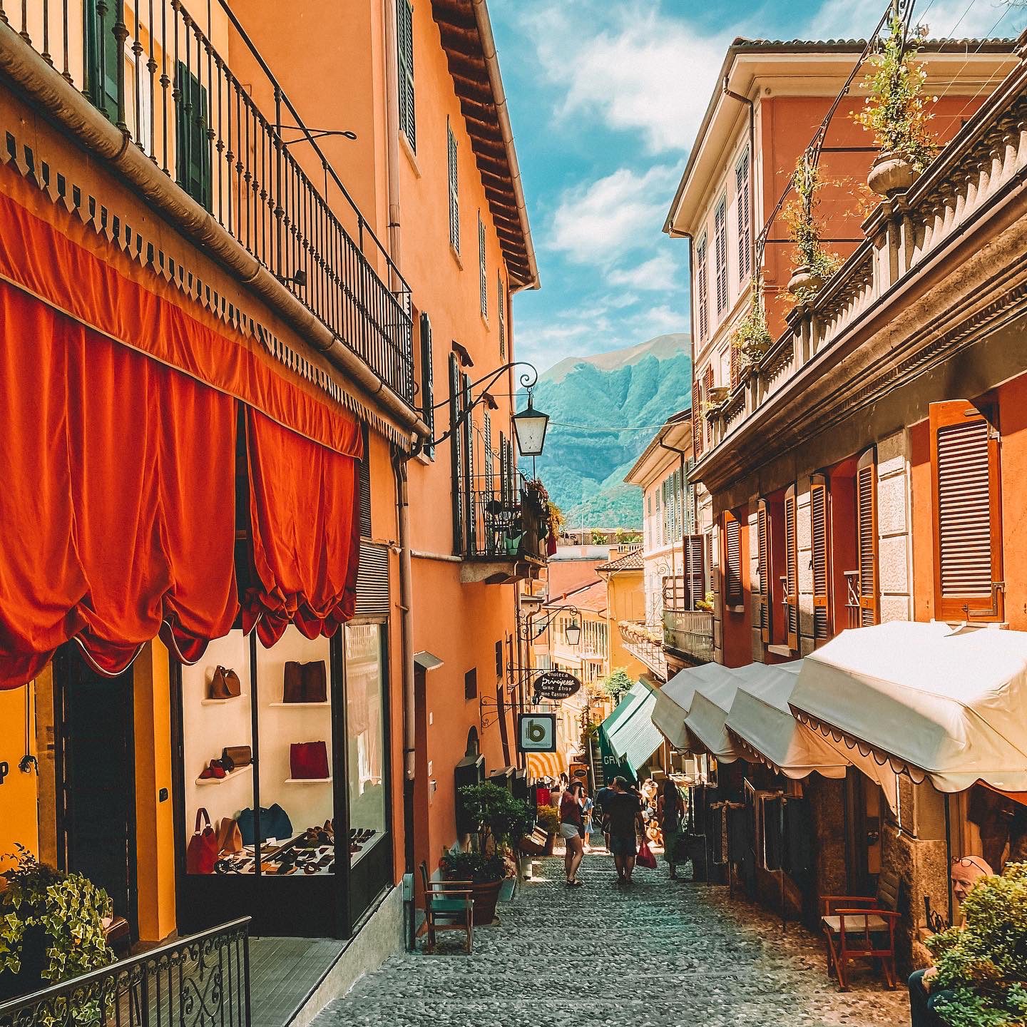 An Italian cobbled street lined with terracotta buildings with shutters and shop awnings.