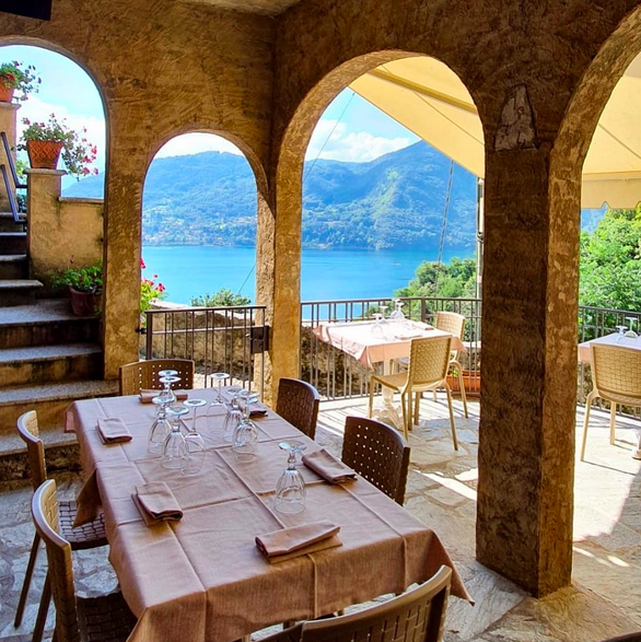 A restaurant terrace set on a hillside with views of a blue lake and mountains in between the stone archways. The tables are set with pink table cloth, pink napkins and glassware.