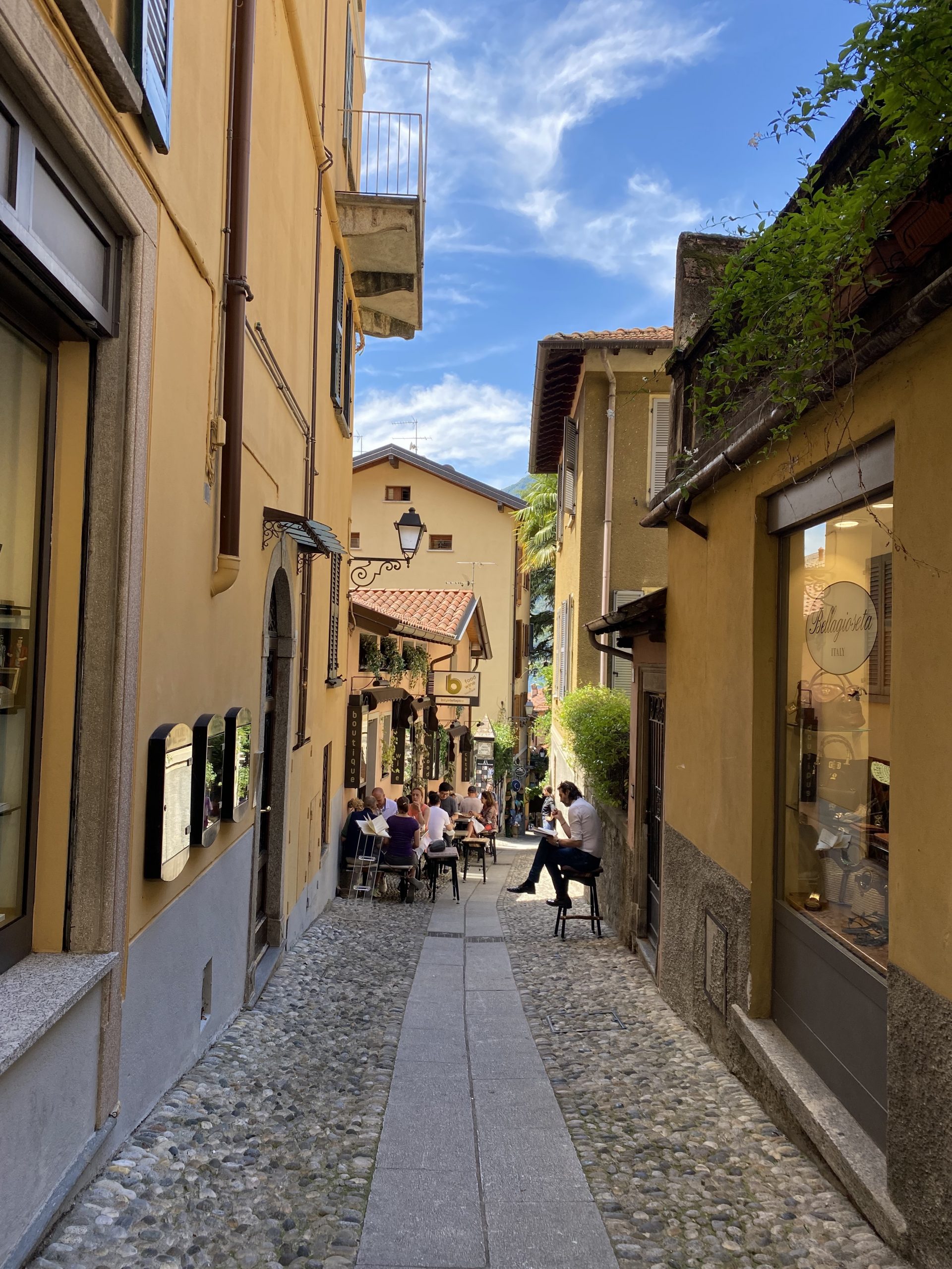 A cobbled passageway leading downhill with yellow buildings on each side and people eating outside a restaurant on the left