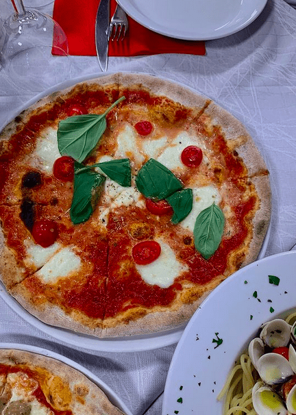A plate of margherita pizza with fresh tomato and basil on a table with a white table cloth.
