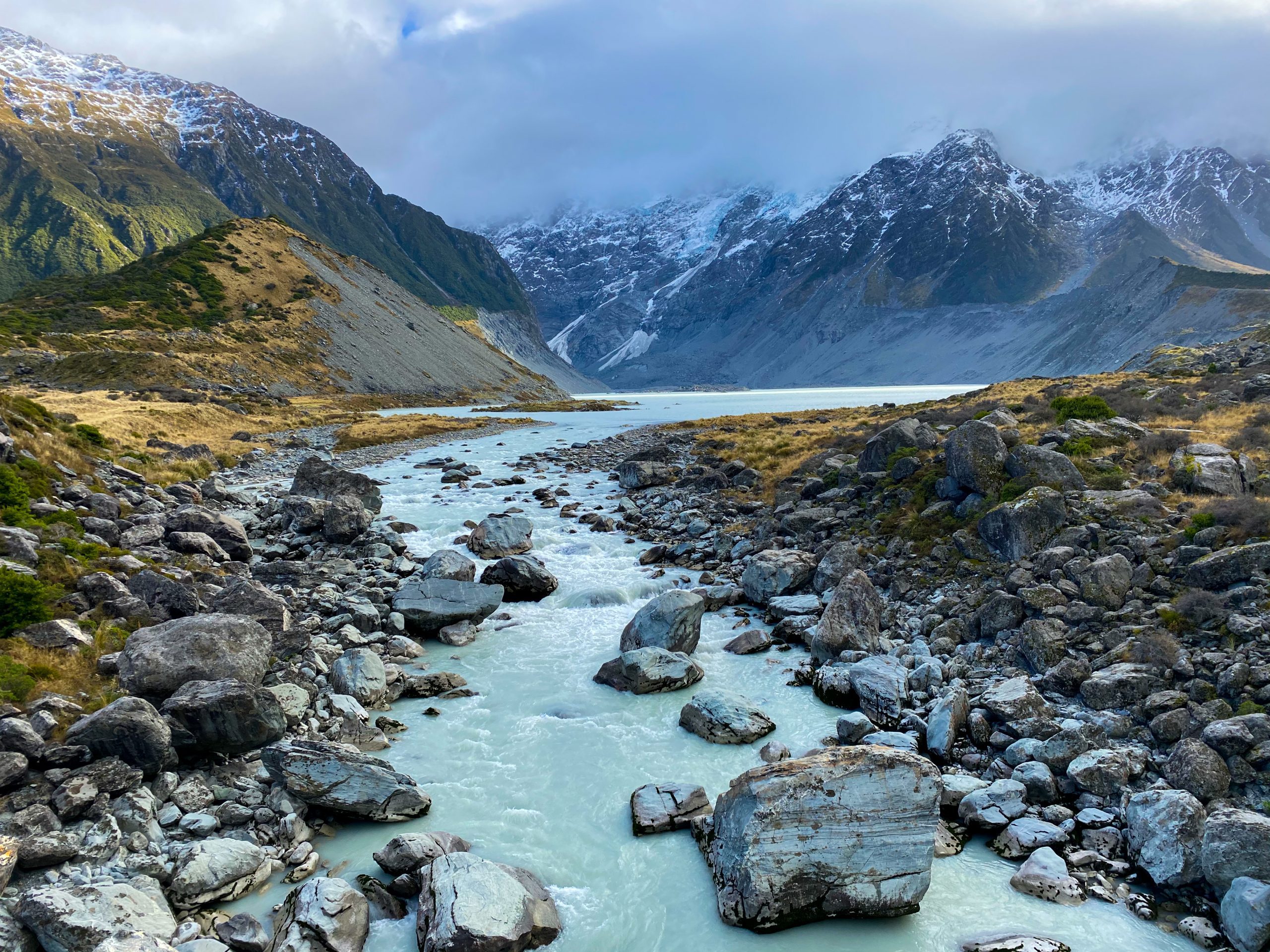 A glacial river running through rocks with snow-capped mountains in the background and fog.