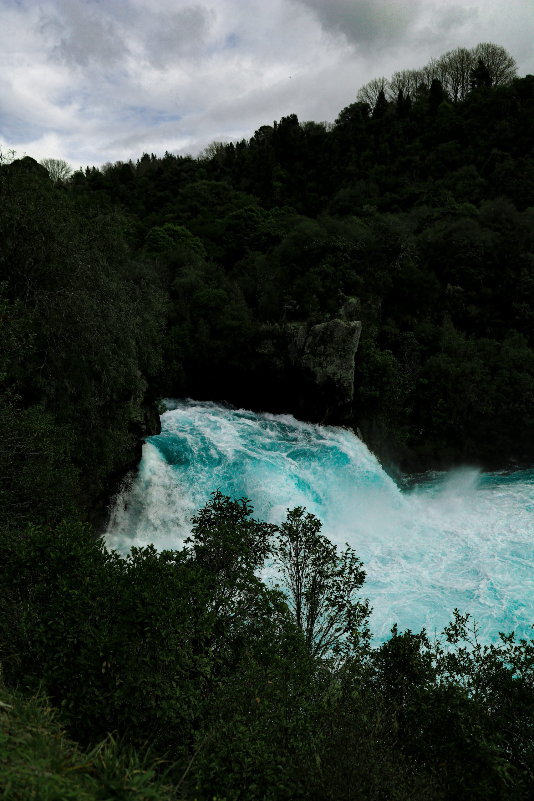 A strong waterfall cascading down into a pool creating blue foam, surrounded by trees.