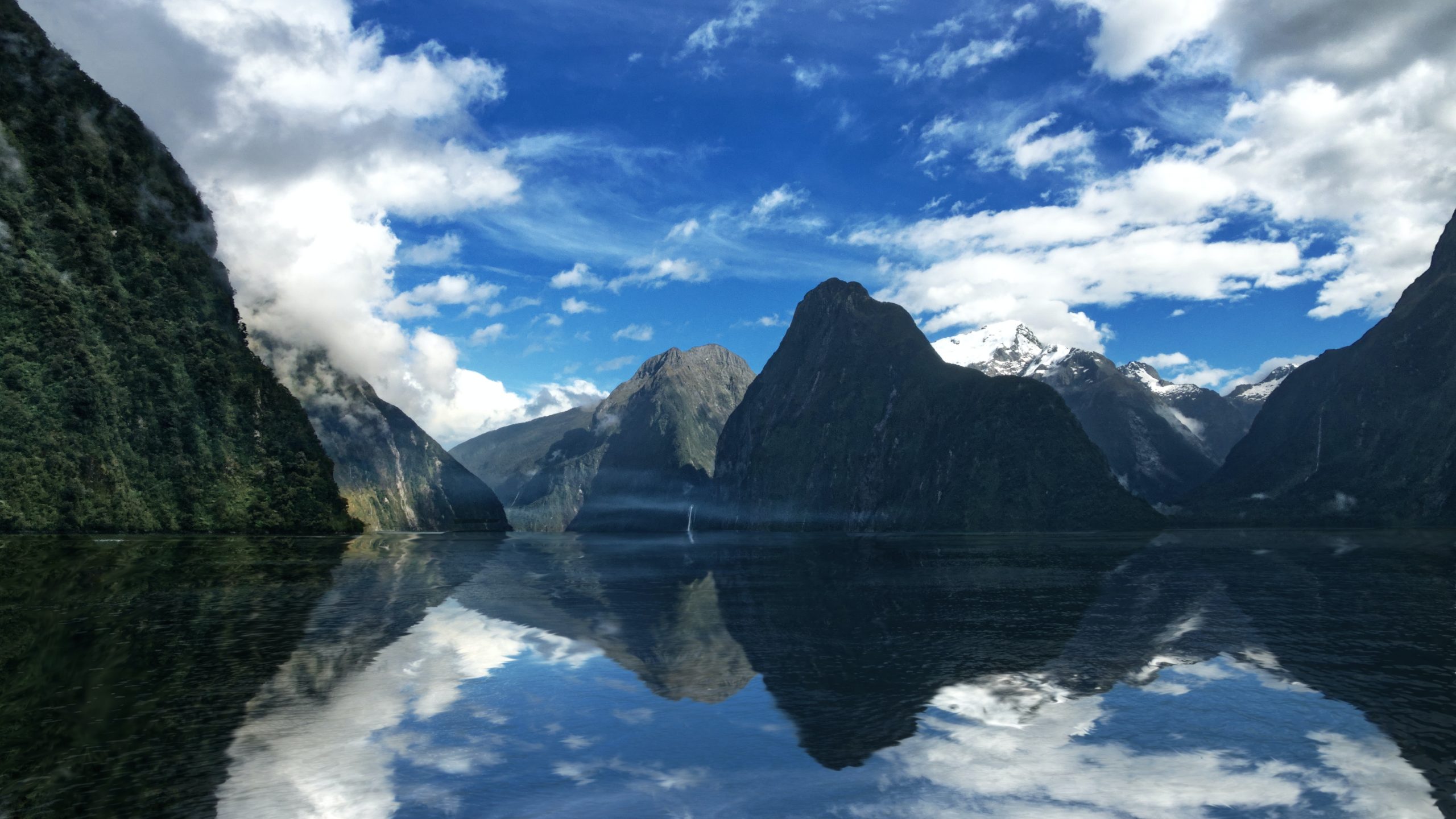 A fiord surrounded by steep mountains which are reflected in the glassy water.