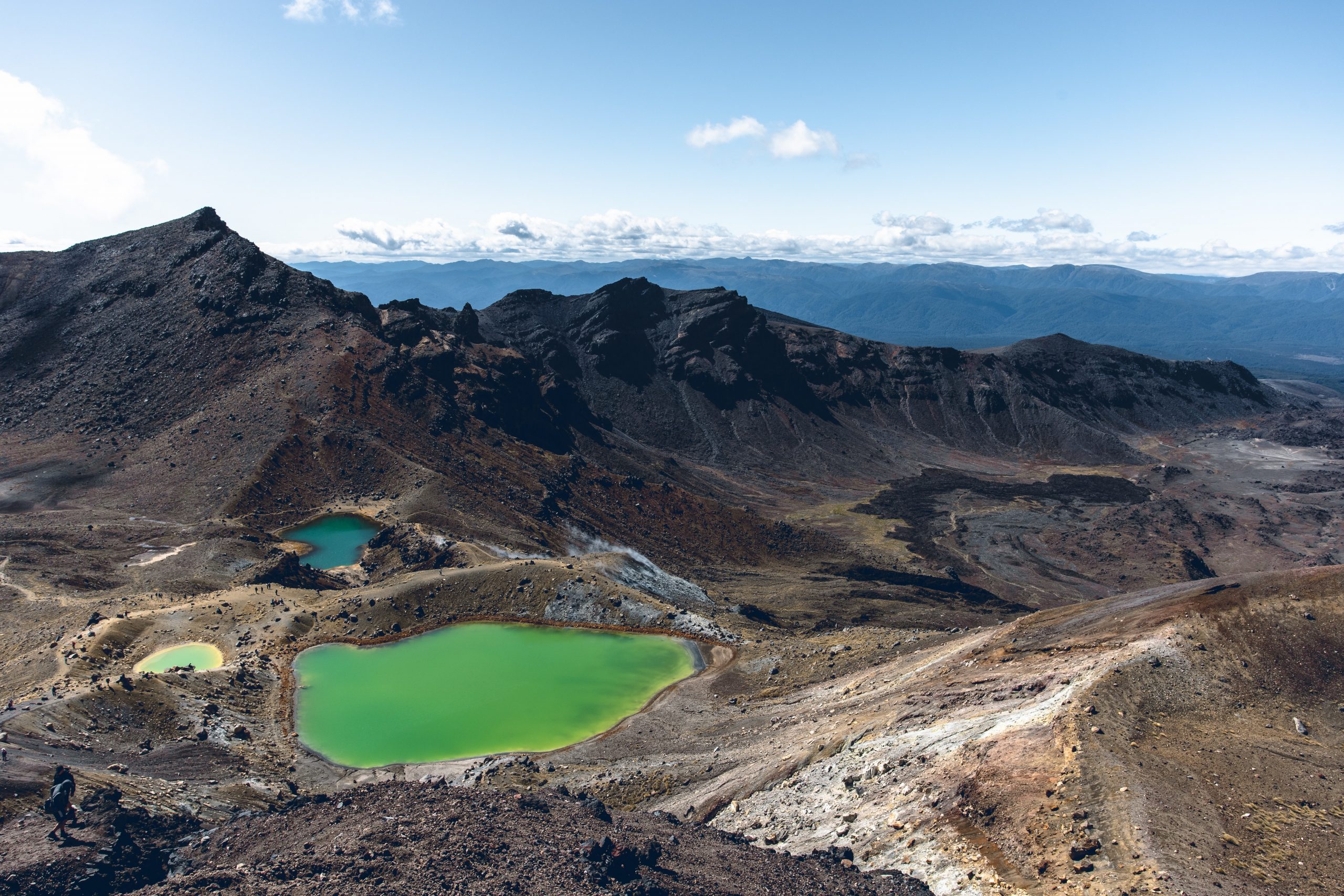 A rocky volcanic landscape of dark brown peaks and green lakes shown from a high viewpoint.