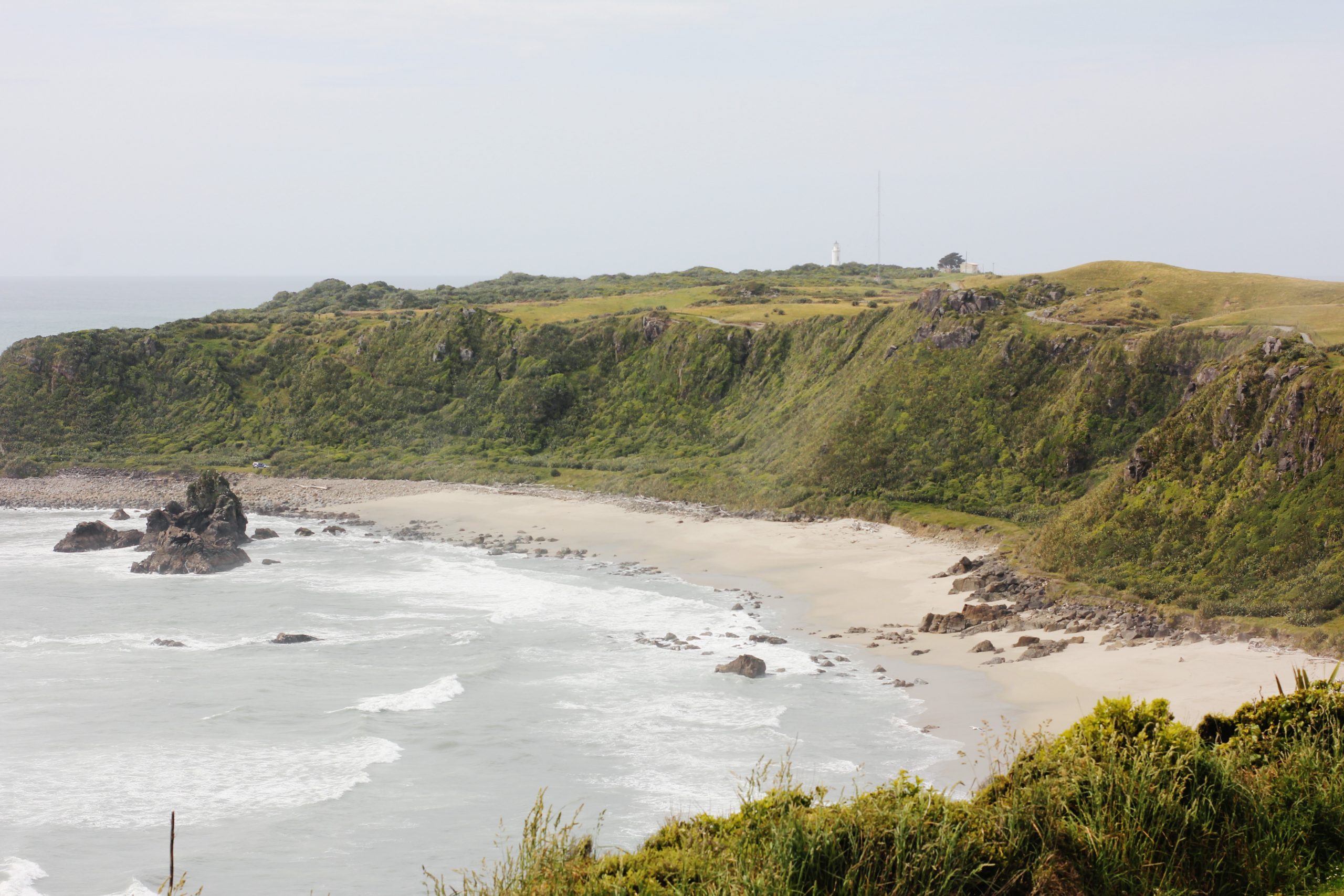 A rocky beach with moderate waves flanked by grassy headland.