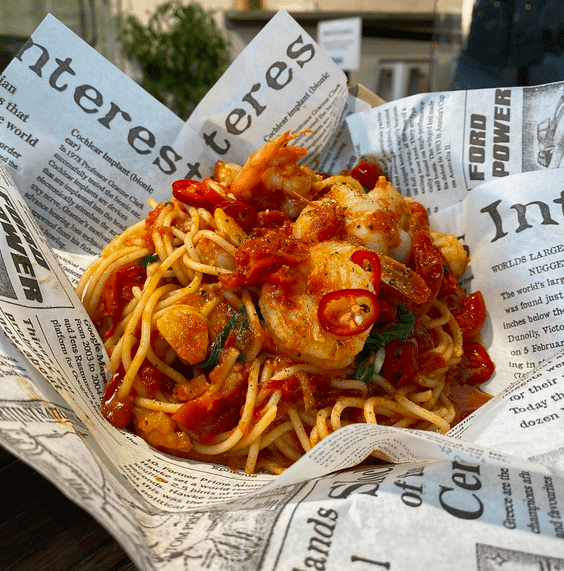 A tomato, chilli and king prawn spaghetti dish served in newspaper.