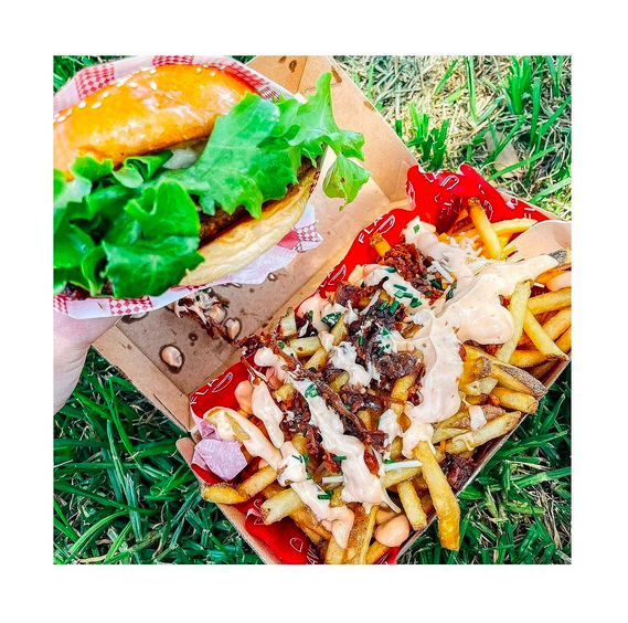 A burger and some loaded fries in a cardboard box on some grass.