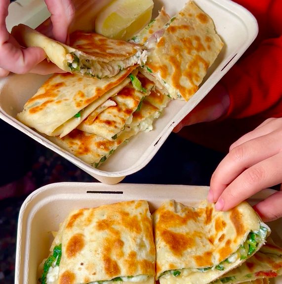 Two hands reaching into two white trays filled with turkish stuffed flat bread.