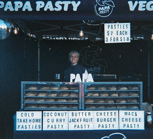 A person in front of two cabinets filled with pasties, with the different varieties displayed on neon signs in the foreground.