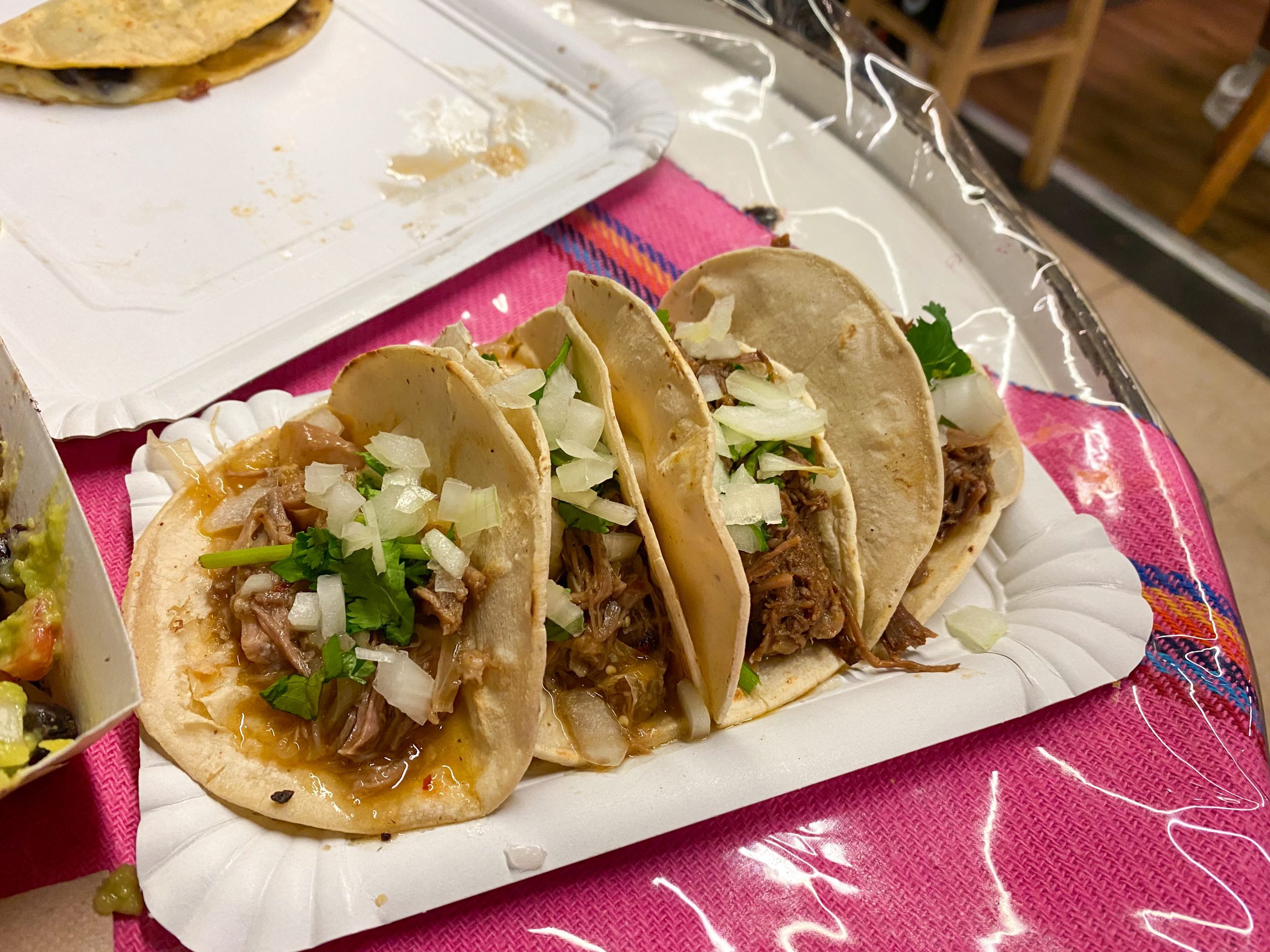 A paper plate filled with soft shell tacos with a clear plastic sheet underneath.