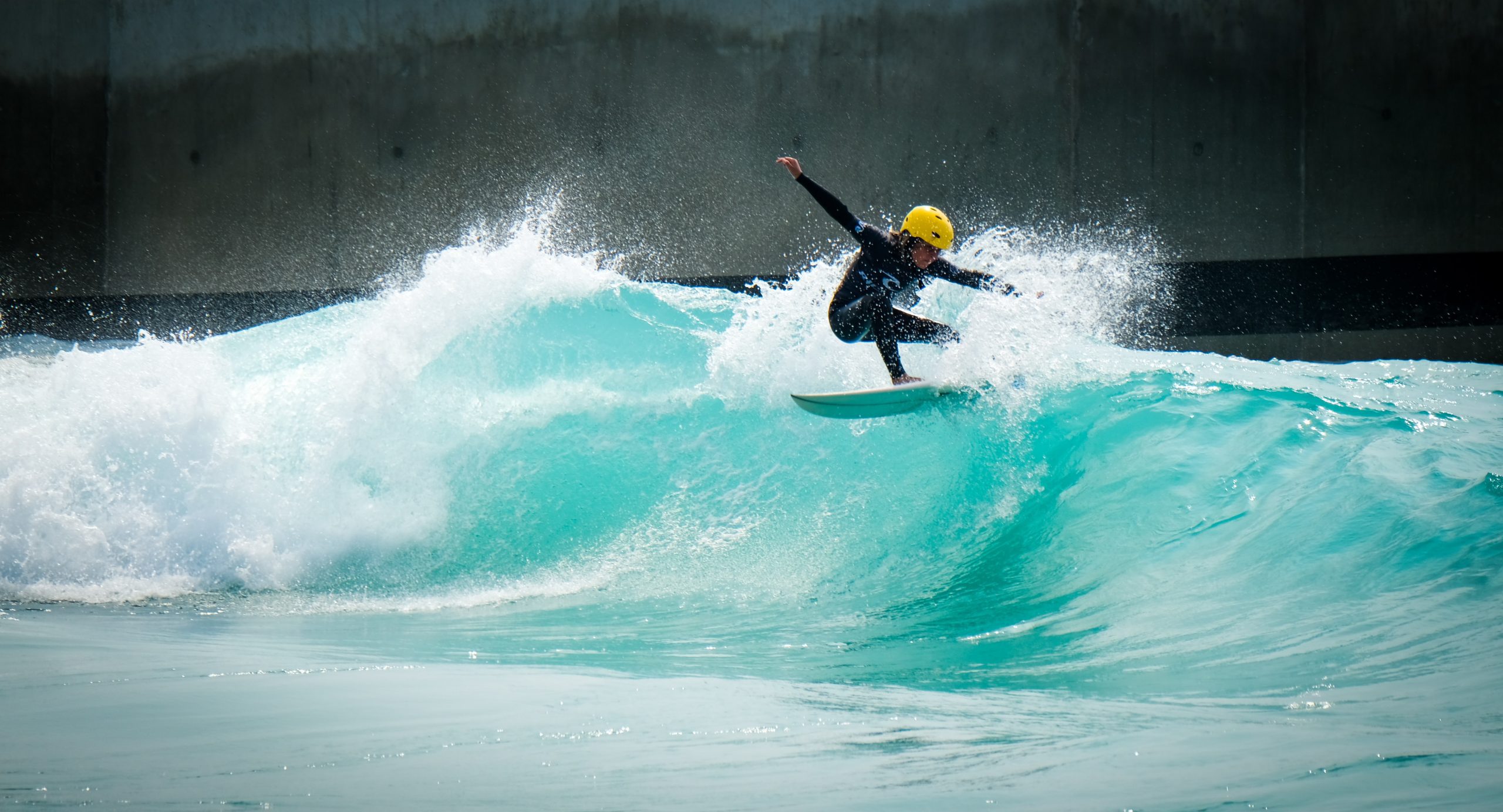 A boy with a yellow helmet surfing a wave at an artificial wave park.