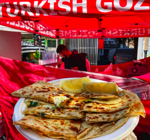 A paper plate filled with stuffed turkish flat bread and lemon slices in front of a red market stall.