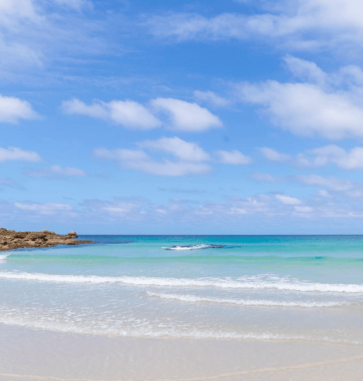 The view of the ocean from a beach with gentle waves and clear blue water against white sand.