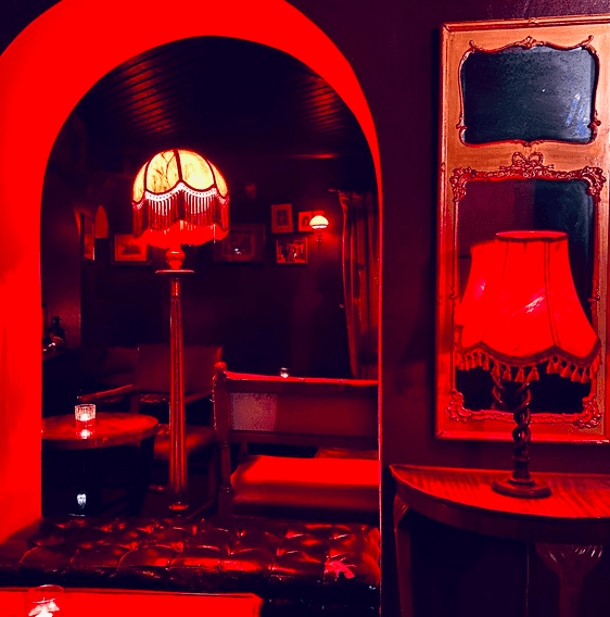 A dark room with red lighting and old fashioned furniture and lamps.