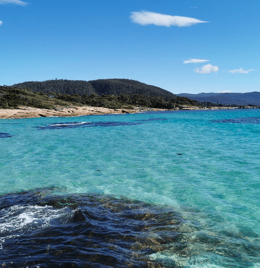 A bay with clear blue water and vegetous hills in the background.